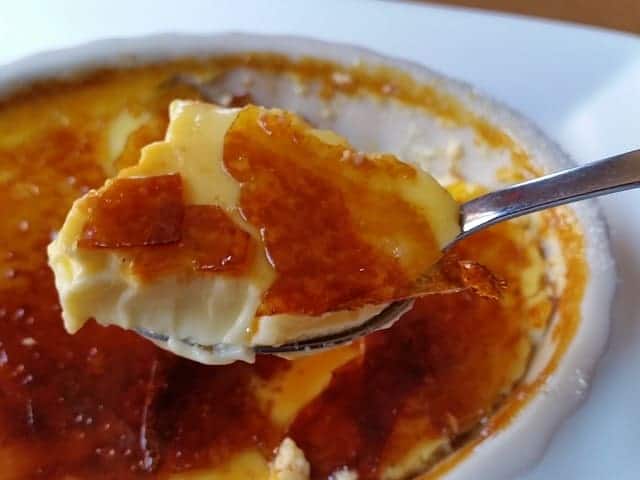 Close up of a spoonful of creme brulee with crunchy caramelized topping and pale yellow custard.