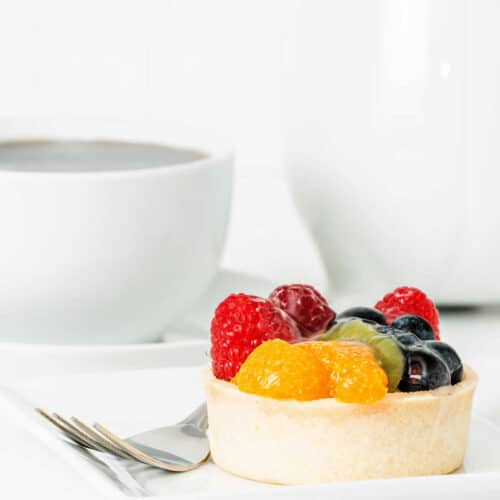 An individual fruit tart with mandarin oranges and berries on a white plate.