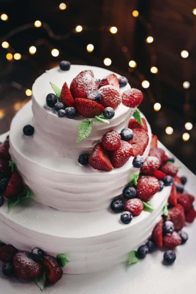 three tiered cake frosted white with berries cascading down the side