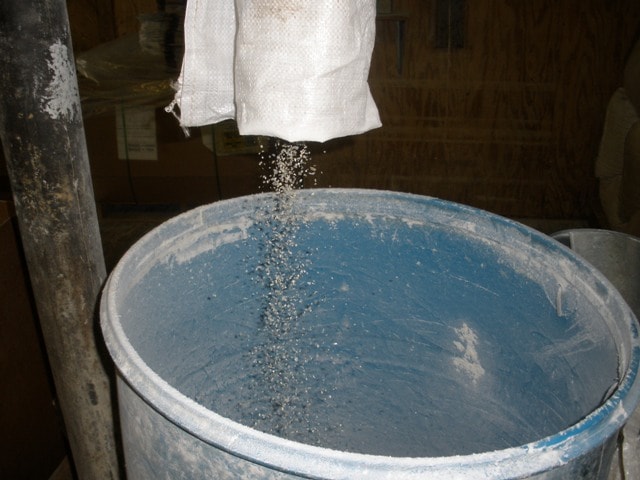 the outsides of the corn kernels falling out of a white chute into a large bucket. This chaff is sold and added to chicken feed.