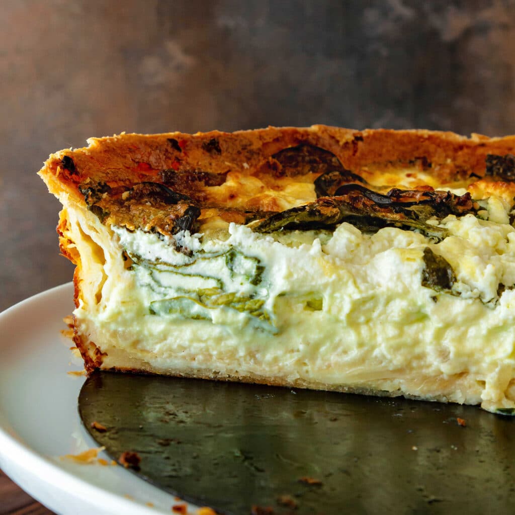 A close up of the cut side of a quiche showing spinach, onions, and goat cheese suspended in the custard rather than fallen to the bottom of the quiche.