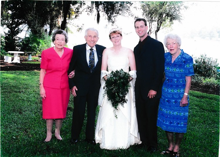 A bride and groom standing in a grass field with their grandparents.