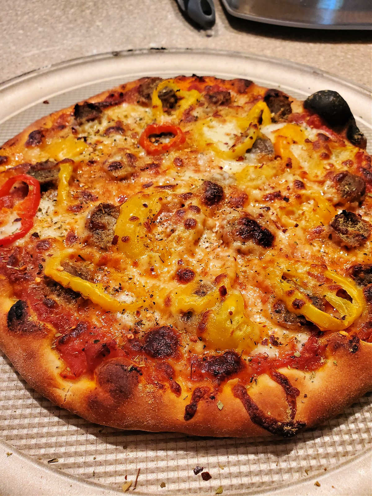 A close-up shot of a baked pizza with cheese, pickled peppers, and sliced meatballs.