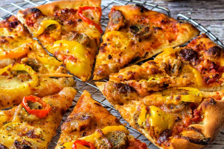 A whole, thin-crust pizza topped lightly with pickled peppers and sliced meatballs, cut into eights and resting on a round cooling rack.