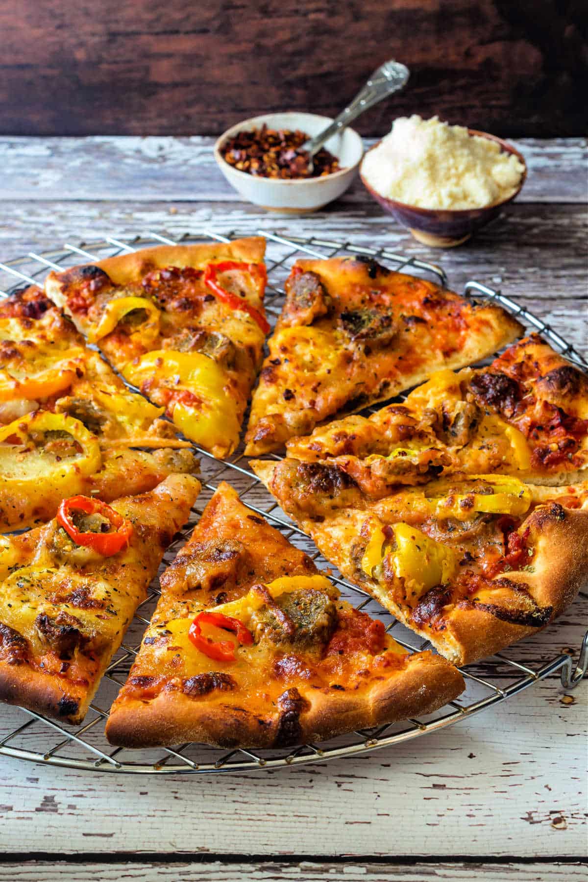 A whole, thin-crust pizza topped lightly with pickled peppers and sliced meatballs, cut into eights and resting on a round cooling rack.