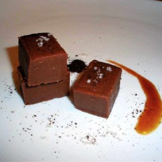 Three pieces of fudge topped with flaky salt and cinnamon on a white plate.