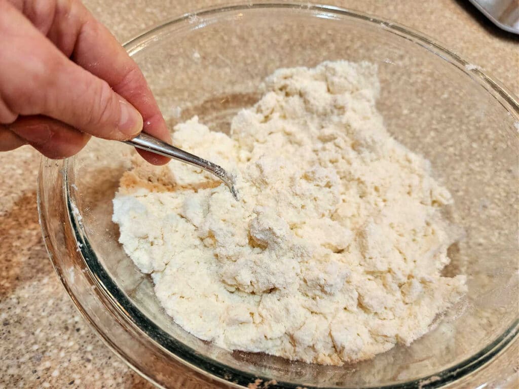 A glass bowl with flour and water in it. I'm using a fork to mix the water into the flour.