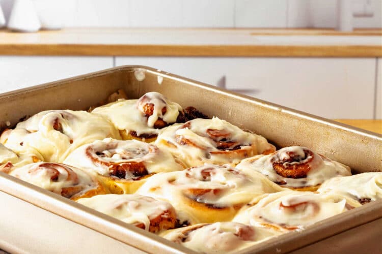 A rectangular pan of frosted cinnamon rolls on a cutting board on a butcher block countertop.
