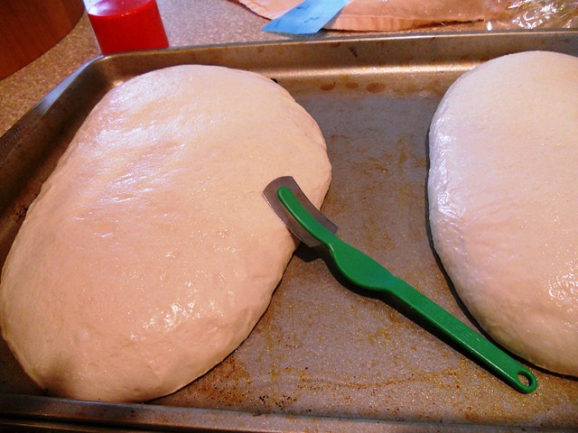 Two loaves of bread dough rising on a metal sheet pan with green lame.
