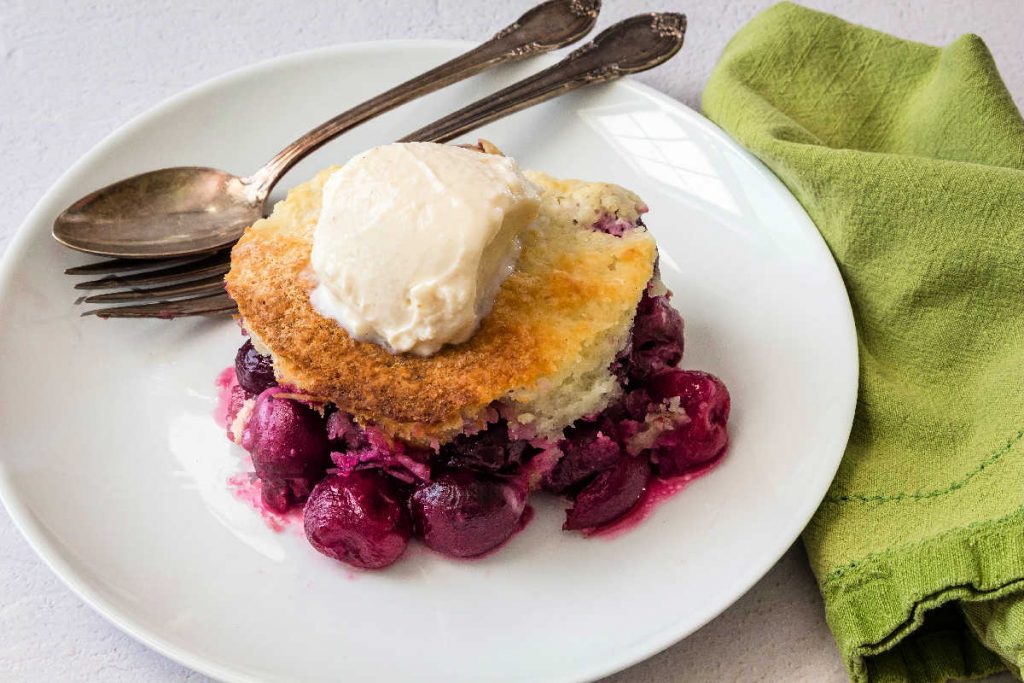 A serving of cobbler topped with vanilla yogurt with a spoon and a fork on the plate.