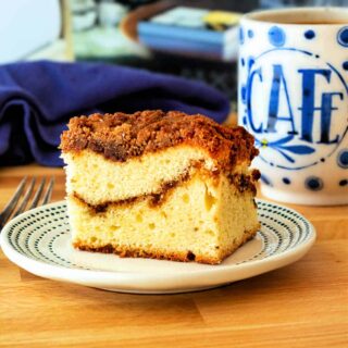 A square of coffee cake on a plate with a mug of coffee.