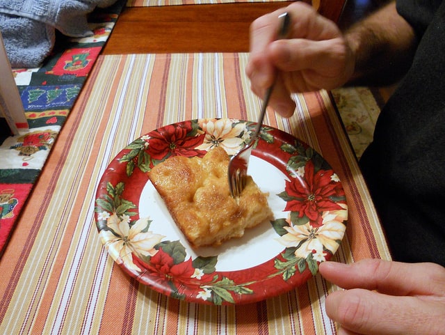 A slice of Moravian sugar cake on a holiday decorated paper plate with a fork in it, ready to take a bite.