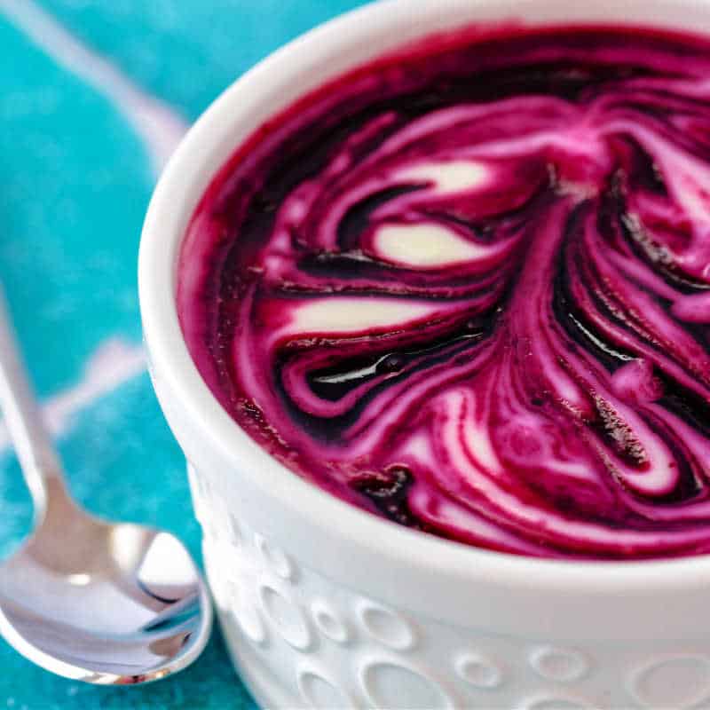A closeup of a ramekin of lemon dessert swirled with brilliant, bright purple blueberry sauce.