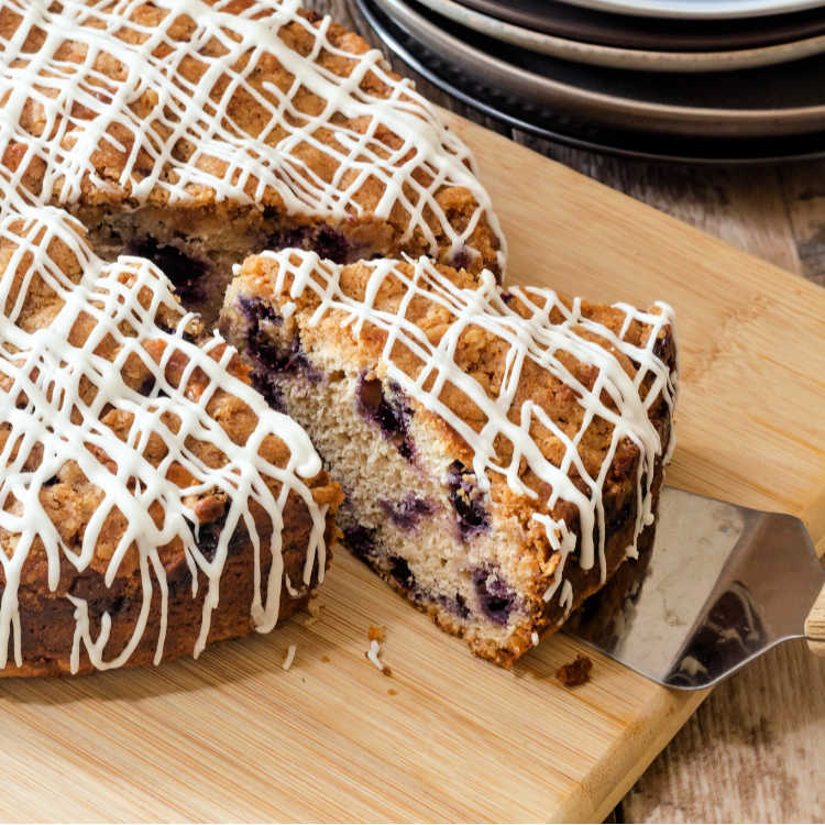 Brown butter blueberry coffee cake with glaze drizzled on it on a cutting board with one slice cut out of it.