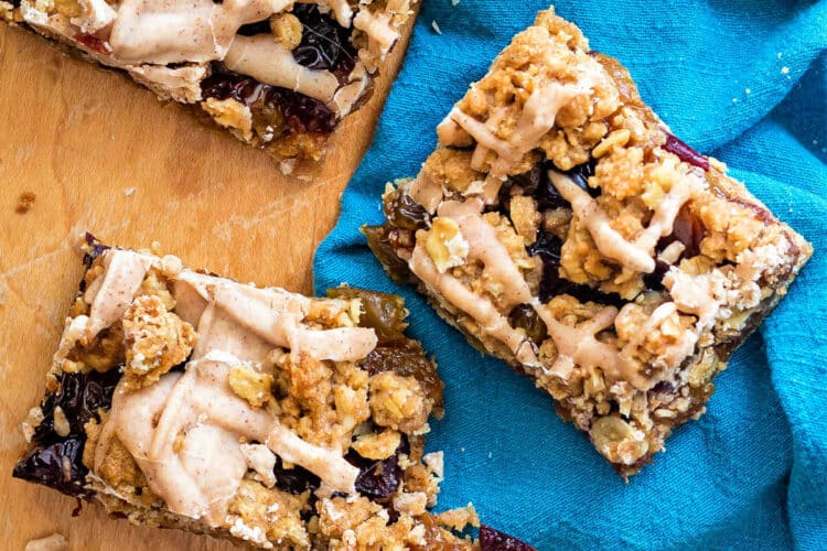 overhead shot of rectangular bar cookies with cinnamon glaze drizzled on top. The tops have blobs of oatmeal dough baked on top and you can see plumped, dried fruit peeking through.