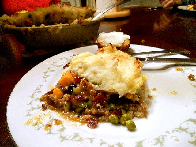 A slice of thanksgiving turkey shepherd's pie with stuffing crust on a white plate along with a buttered corn muffin.