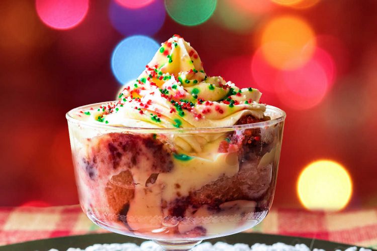 A bowl of Christmas trifle topped with whipped cream and red and green sprinkles on a glass plate.