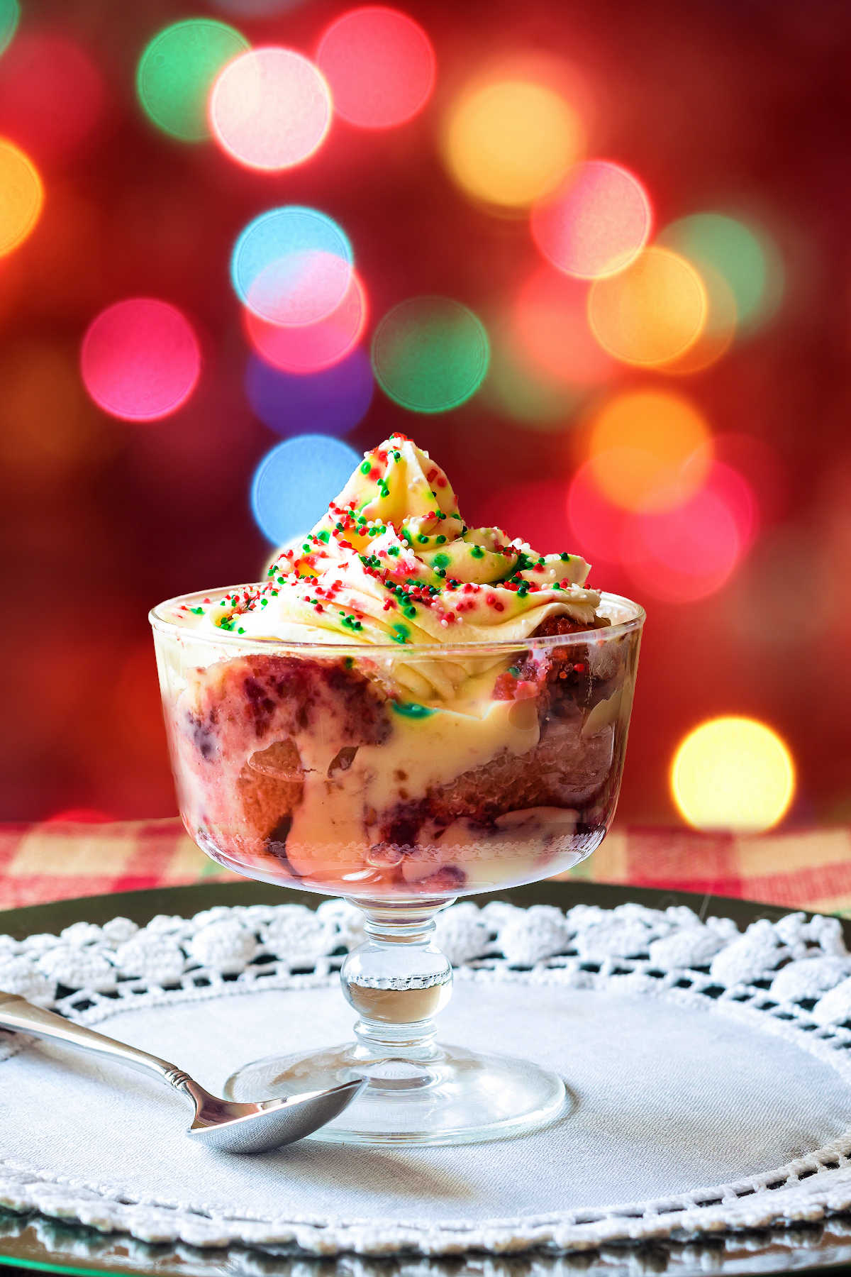 A bowl of Christmas trifle topped with whipped cream and red and green sprinkles on a glass plate.