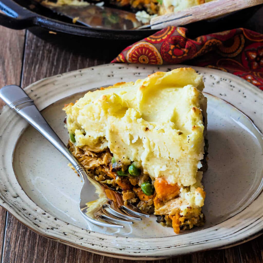 A slice of turkey shepherd's pie with stuffing crust and mashed potato topping on a plate with a fork.