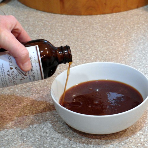 Pouring vanilla into finished caramel sauce in a white bowl.