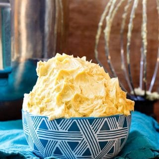 caramel buttercream frosting in a blue bowl with the mixer bowl and whisk in the background