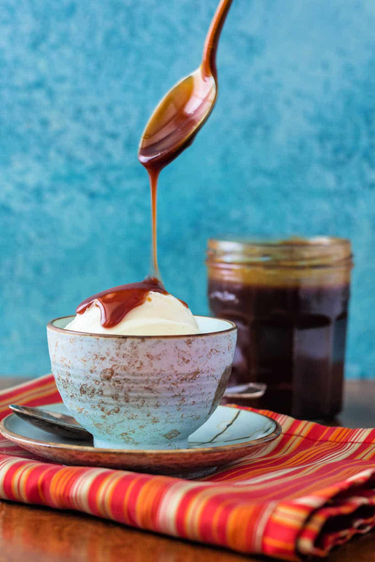 A spoon drizzling caramel sauce over ice cream. The jar of caramel sauce is in the background.