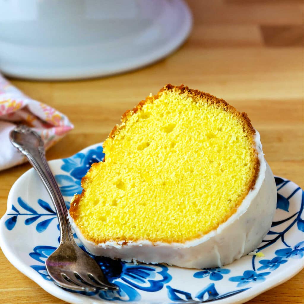 A bright yellow slice of lemon pound cake on a blue-patterned plate.