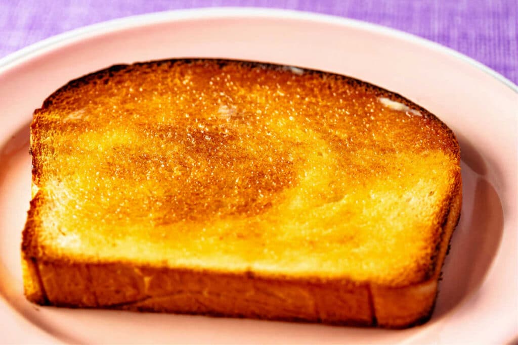 A piece of beautifully toasted white bread with butter on it.