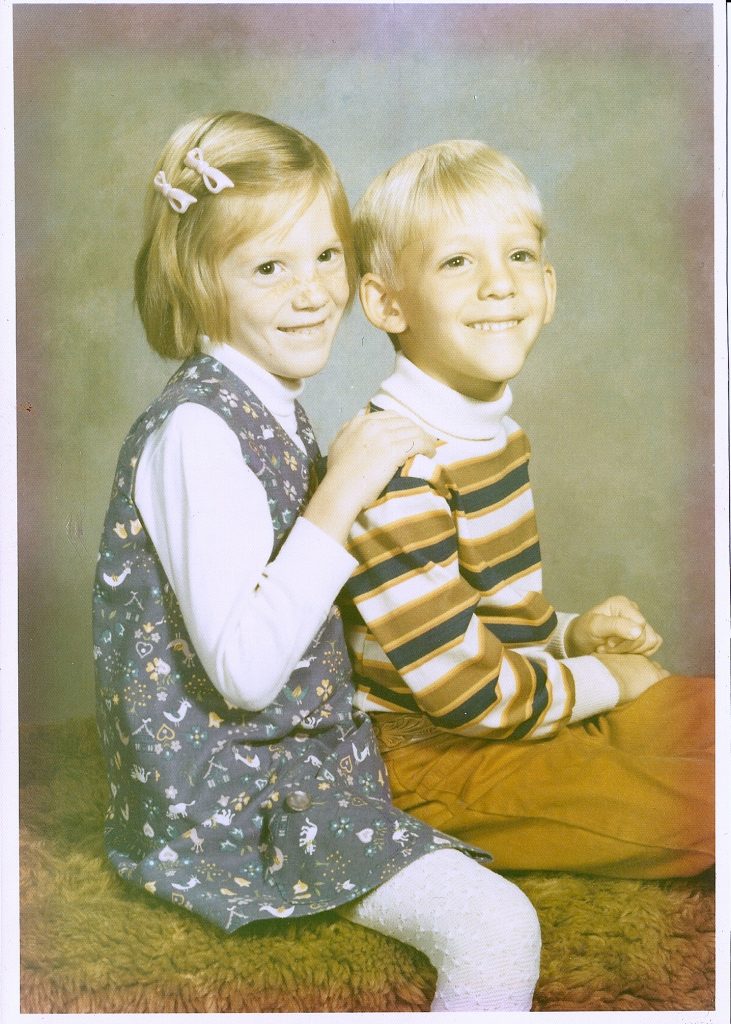 A photo of a girl and a boy sitting together on a carpet-covered bench. Taken in 1971.
