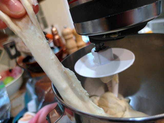 Bread dough being pulled into a long stretchy piece from the mixer.