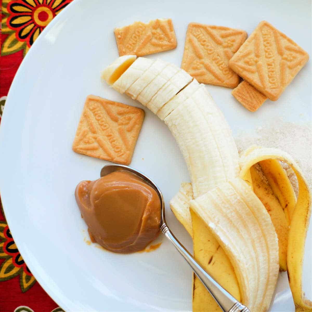An overhead shot of a sliced banana, some Lorna Doone cookies, and a spoonful of dulce de leche on a white plate.