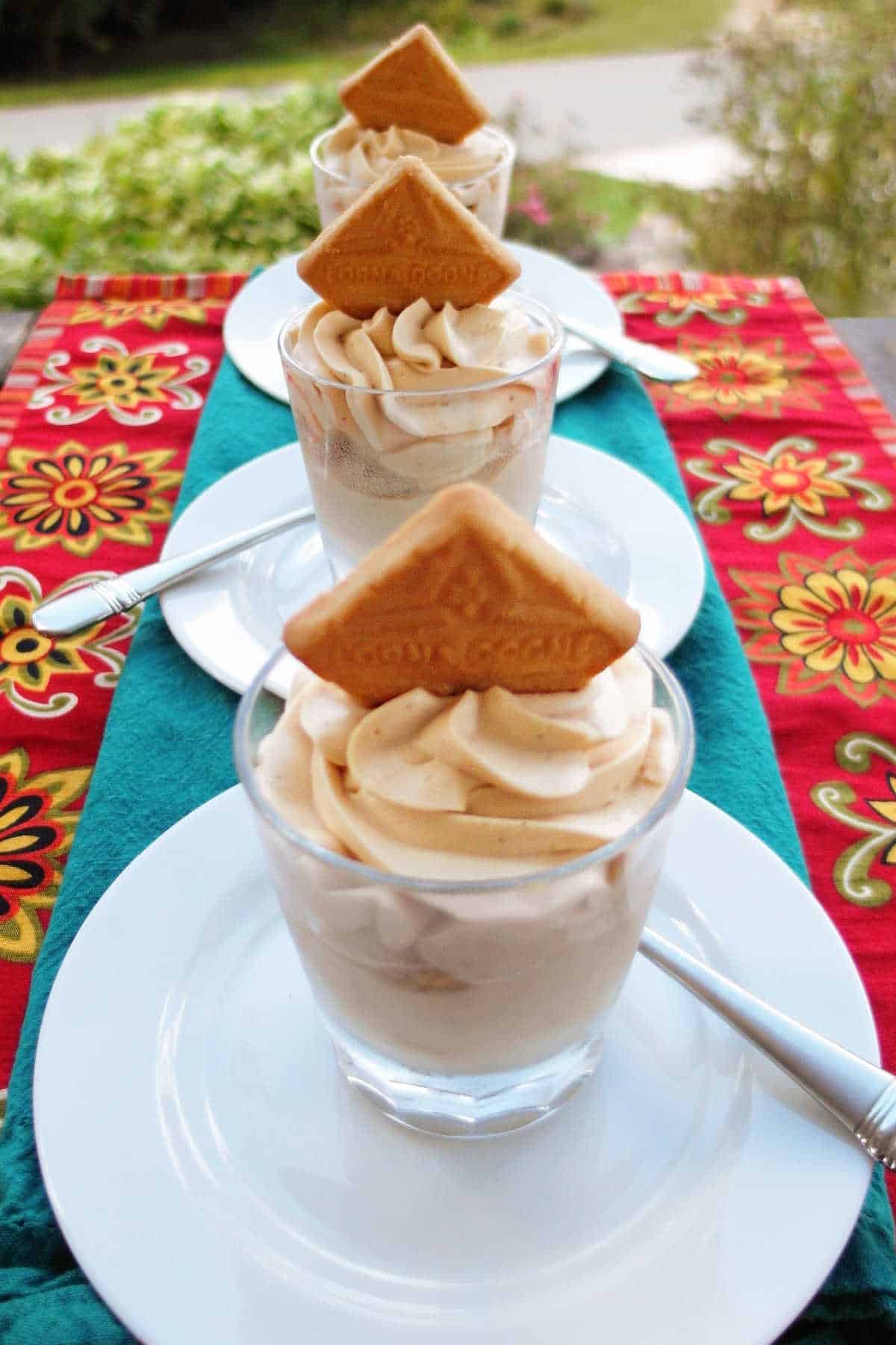 Three small glasses filled with roasted banana pudding and topped with a Lorna Doone cookie.