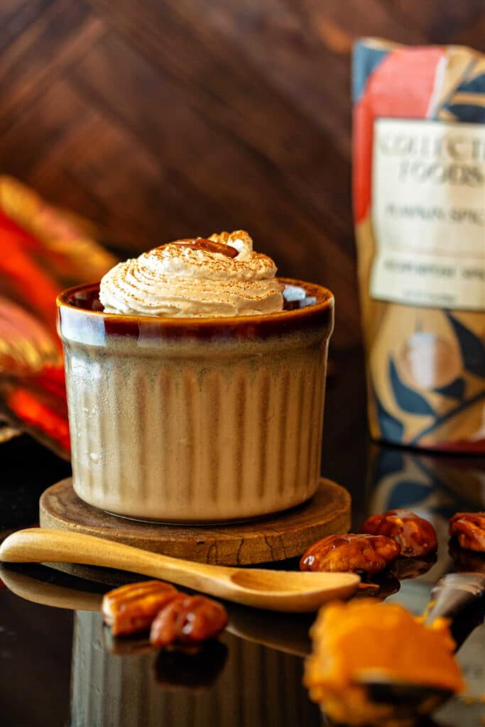 A brown ramekin of pumpkin pudding topped with spiced whipped cream and a maple-glazed pecan.