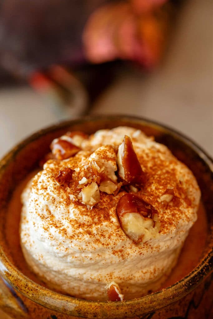 A ramekin of pumpkin pudding topped with whipped cream and chopped pecans.