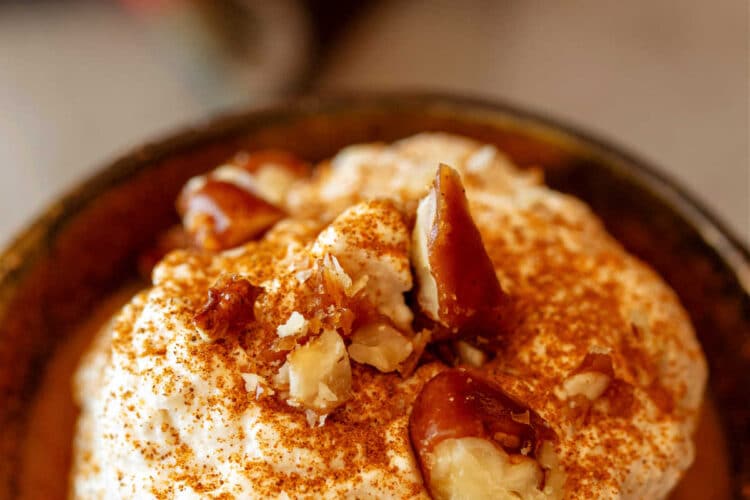 A ramekin of pumpkin pudding topped with whipped cream and chopped pecans.