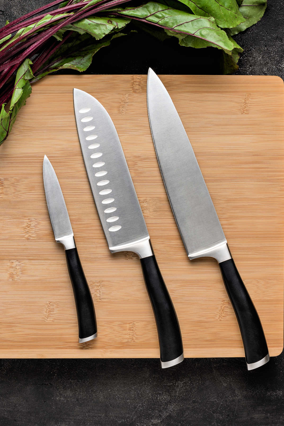 An overhead shot of 3 kitchen knives on a cutting board.