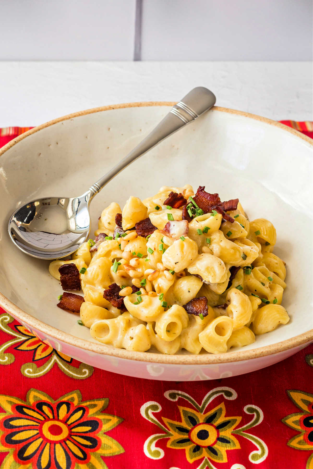 A bowl of fontina mac and cheese topped with bacon pieces and pine nuts.