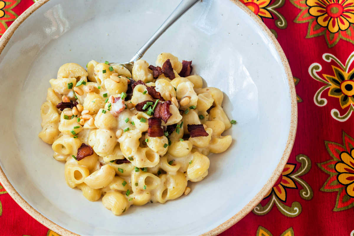 An overhead shot of goat cheese mac and cheese with chives, bacon, and pine nuts.