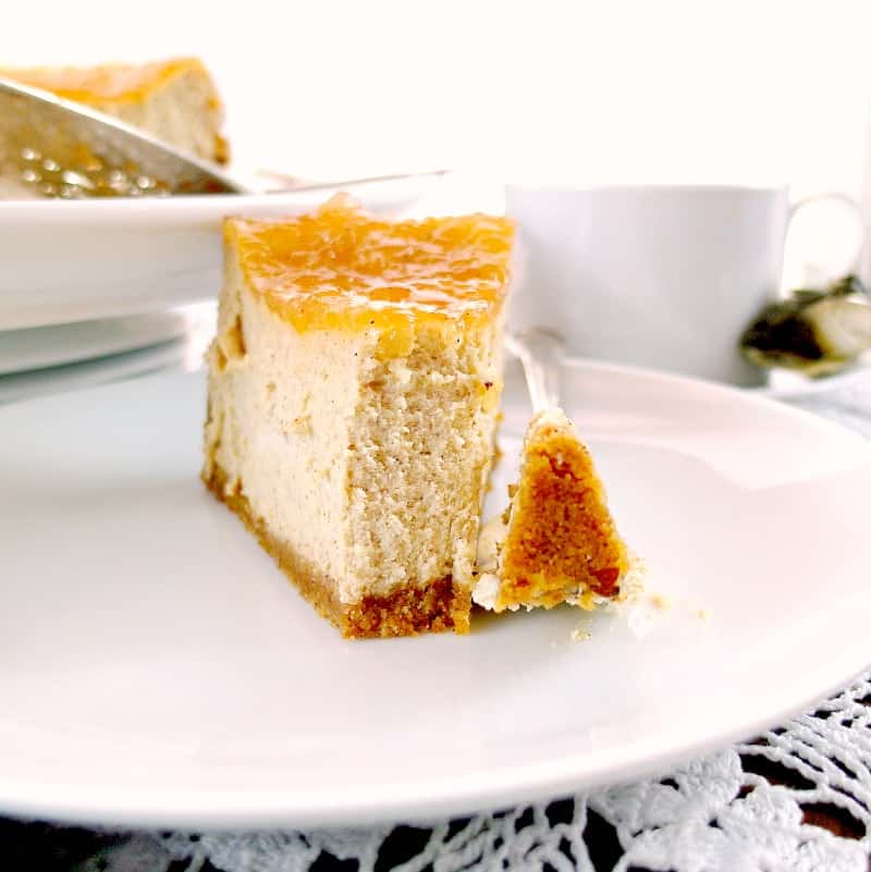 A slice of cinnamon buttermilk cheesecake with apple pie topping on it on a white plate with a bite on a fork.