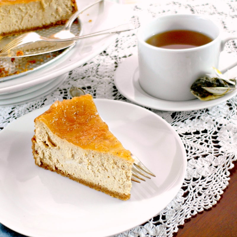 A slice of cinnamon buttermilk cheesecake on a white plate with a cup of tea.