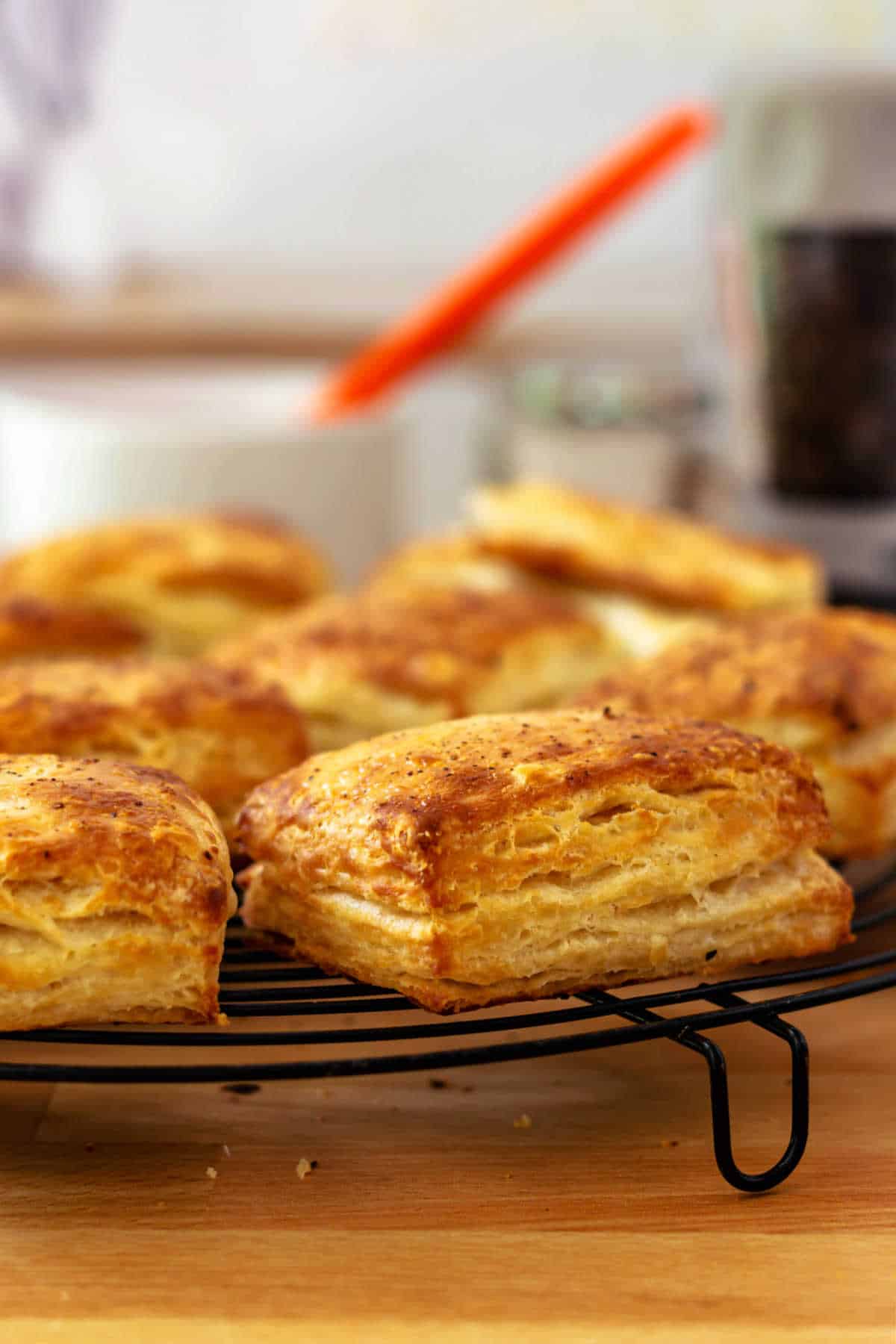 Several golden-brown biscuits coolign on a round, black wire rack on a butcher block surface.