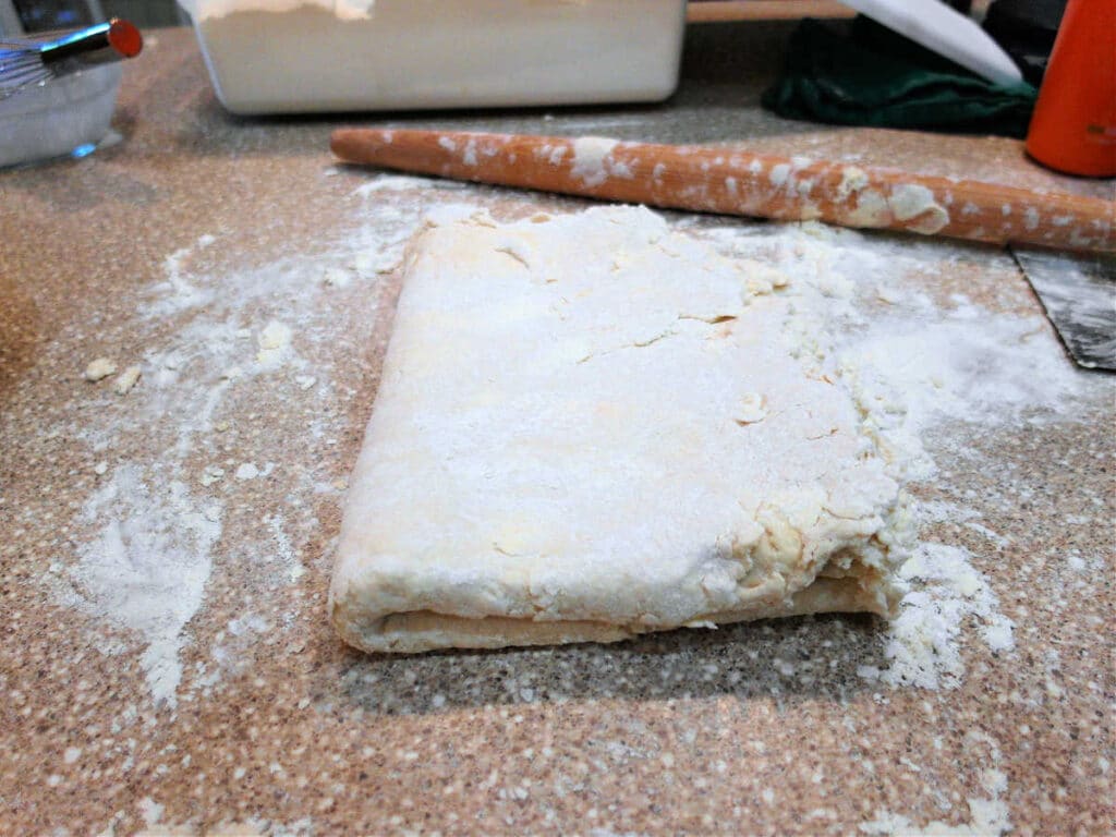 Biscuit dough that has been rolled and folded several times and is now nice and smooth although some pieces of butter still show up in the dough.