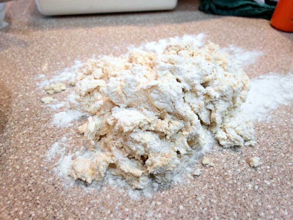 A very messy pile of shaggy biscuit dough on a counter. Some flour is sprinkled on the top.