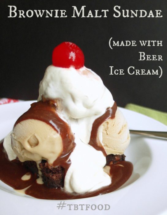 Brownie Malt Sundae (made with Beer ice cream). Photo shows a sundae with scoops of light brown ice cream with whipping cream on top an chocolate sauce melting down it. All sit on a brownie. A maraschino cherry is on top. 