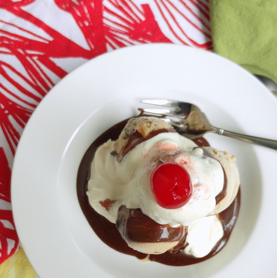 Overhead view of Brownie Malt Sundae in a shallow white bowl. Melting ice cream, whipping cream and chocolate sauce are pooling in the bottom around the brownie. A fork is to the side, ready for eating.