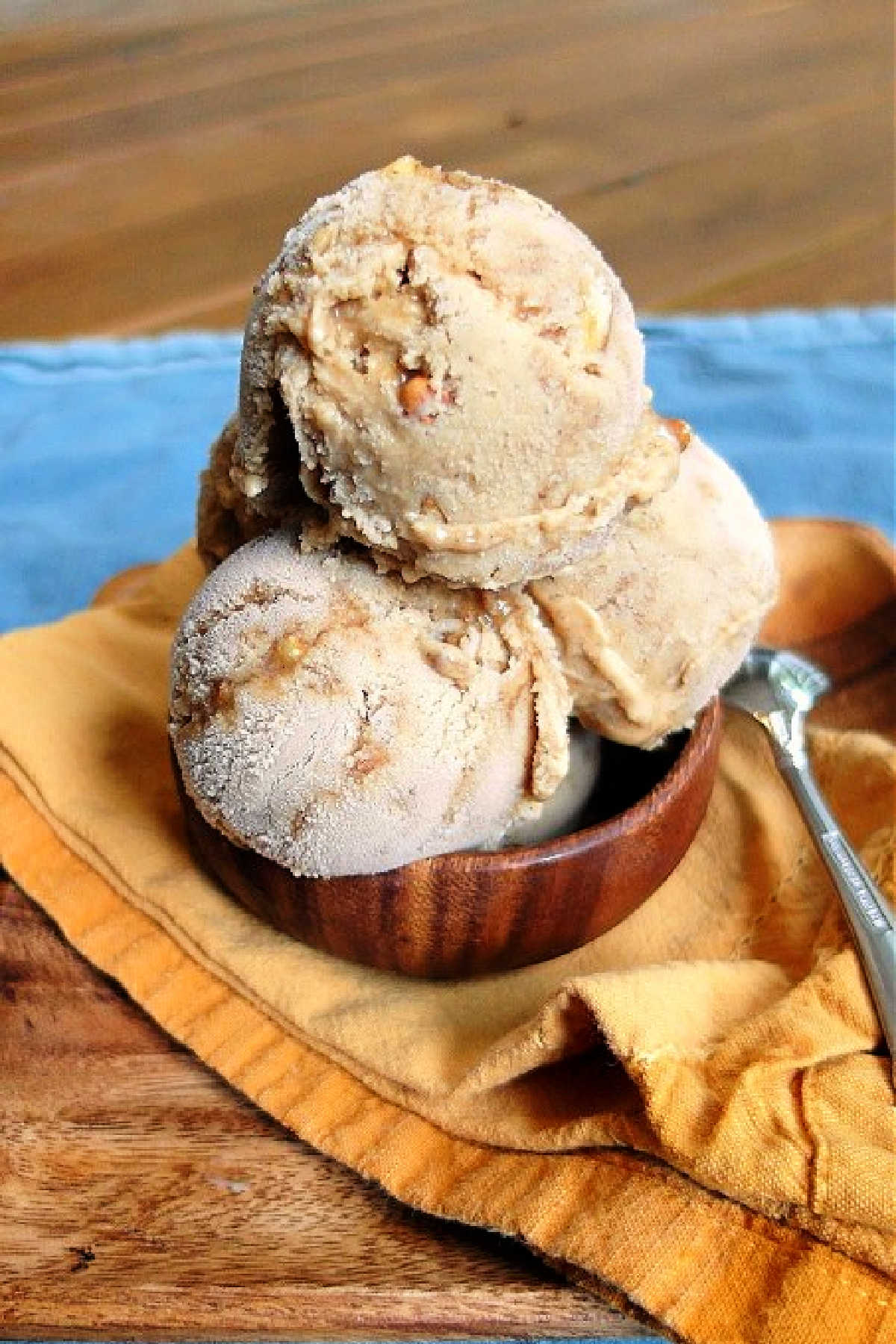 A wooden dish of 3 scoops of pumpkin ice cream with pecan swirls.