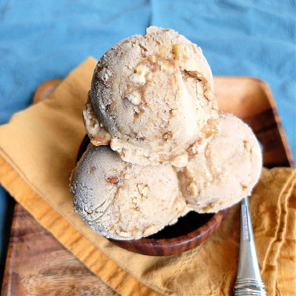 A close-up image of scoops of pumpkin ice cream in a bowl with a spoon.