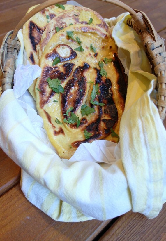 Kashmiri Naan, 3 loaves, in a rattan basket with white and yellow napkin. Fresh herbs sprinkled on bread.