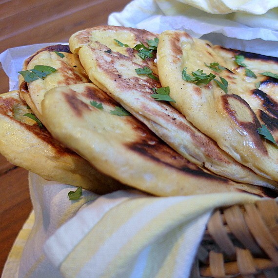 Close up side-view of Kashmiri Naan loaves. 6 loaves stacked in a basket, sprinkled with fresh herbs. 