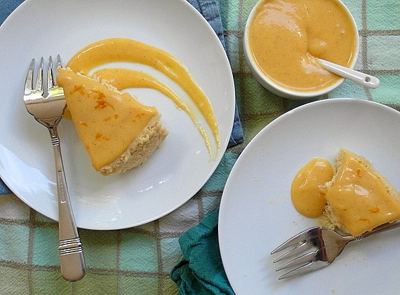 2 plates with pumpkin butter Japanese cheesecake each on white plates. Both have forks. One is missing a bite. A small ramekin of Pumpkin Spice Tangerine Curd is next to the plates with a spoon it it ready for serving. Both slices have curd on top.